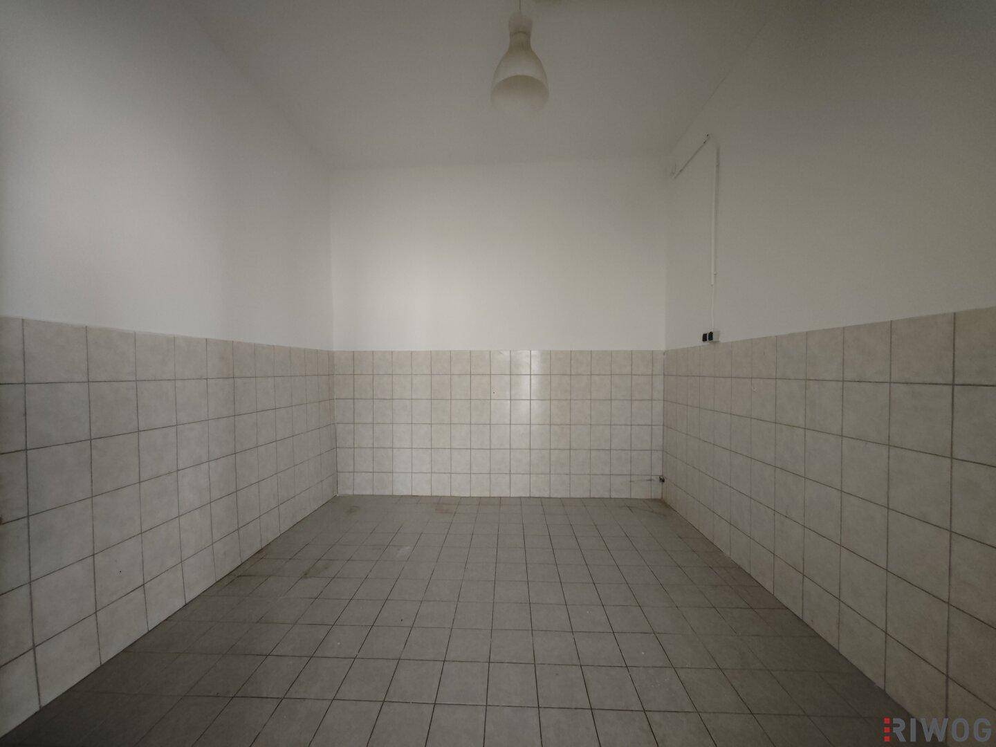 Raum mit grauen Fliesen an Boden und Wänden, ausgestattet mit einer einfachen Deckenleuchte.