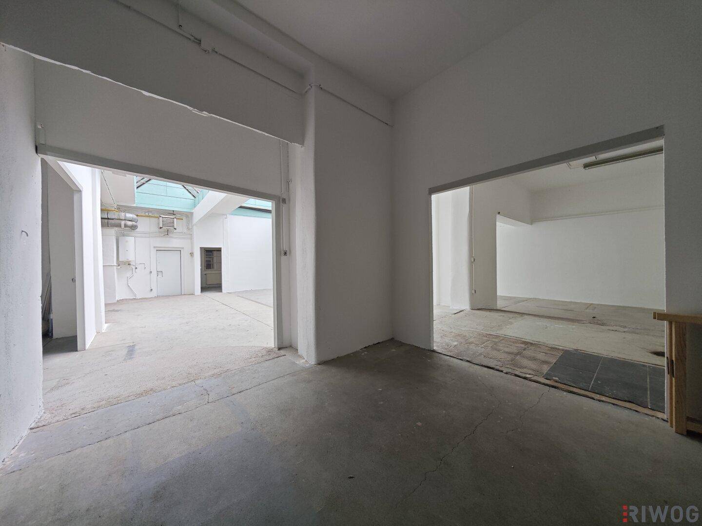Blick von einem Nebenraum in den weitläufigen Hauptgewerberaum mit hohen Decken und Tageslicht.