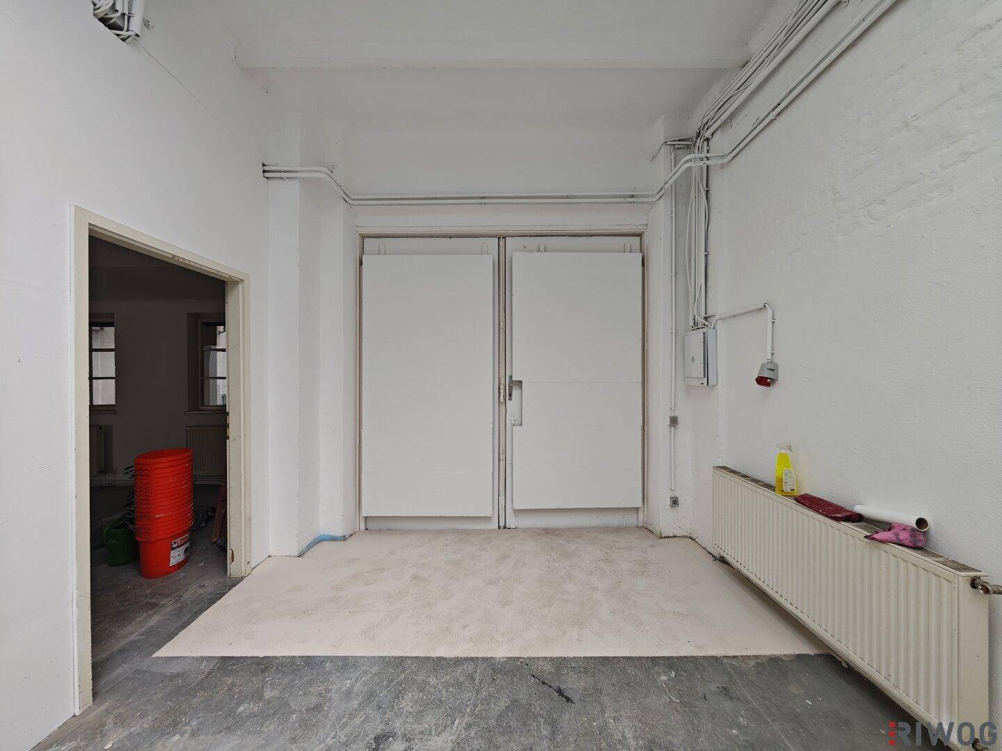 Raum mit großen Doppeltüren, Heizkörper und sichtbaren Rohren, ideal für Anlieferungen.