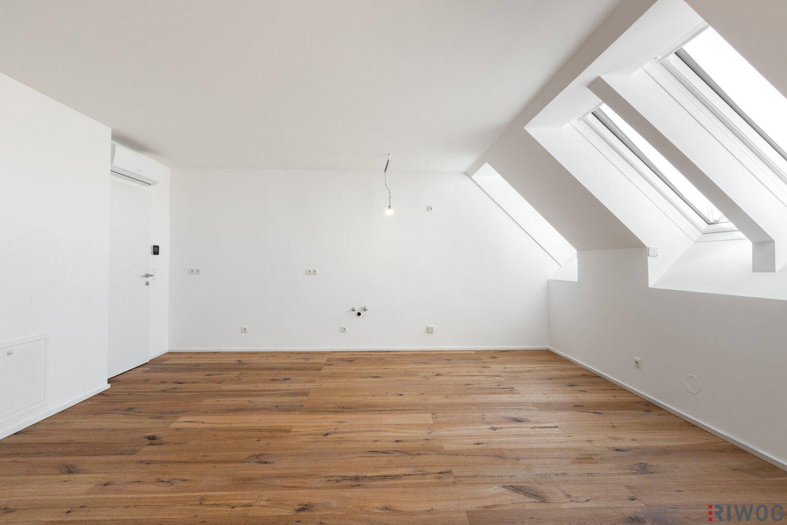 Heller leerer Raum mit Holzboden, Dachfenstern und Klimaanlage.