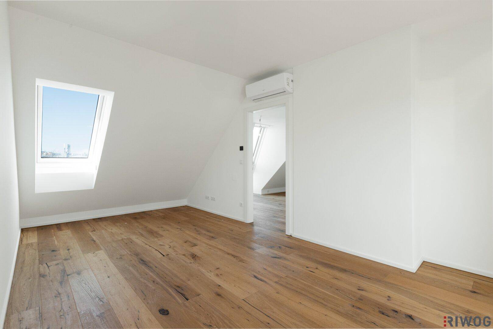 Leerer Raum mit Holzboden, Dachfenster und Zugang zu einem weiteren Bereich.