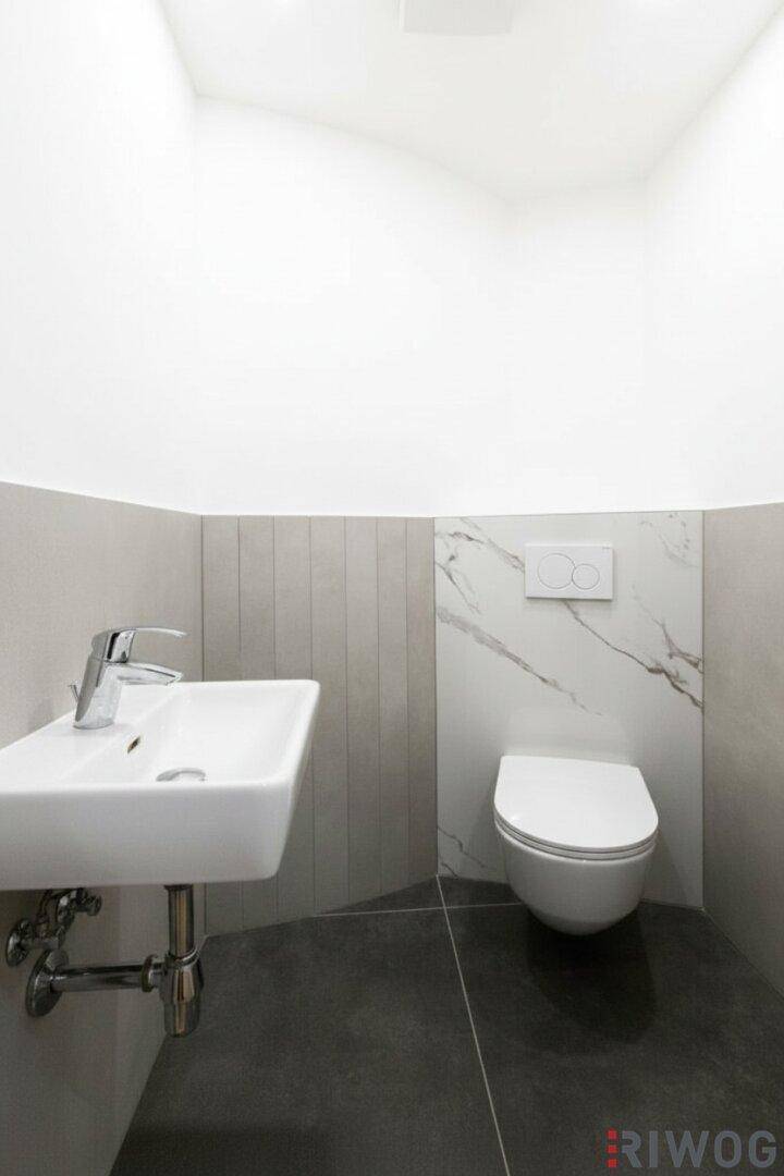 Modernes Gäste-WC mit wandmontierter Toilette, kleinem Waschbecken und Marmorfliesen.