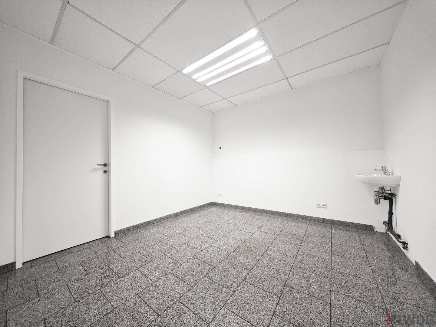 Einfacher Raum mit Granitboden, Waschbecken und weißer Tür.