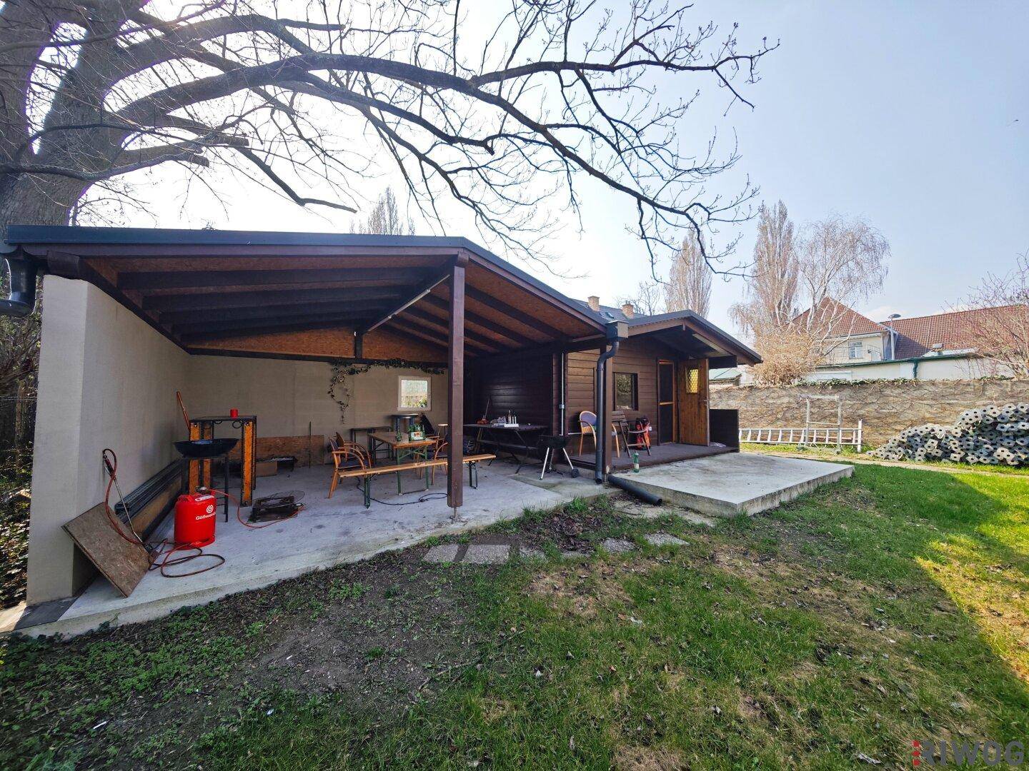 Gartenhaus mit überdachtem Sitzbereich, Grillplatz und Rasenfläche.