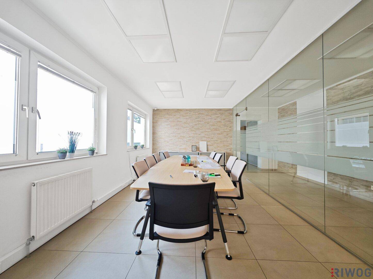 Heller Besprechungsraum mit großem Tisch, Fliesenboden und Fenster für Tageslicht.