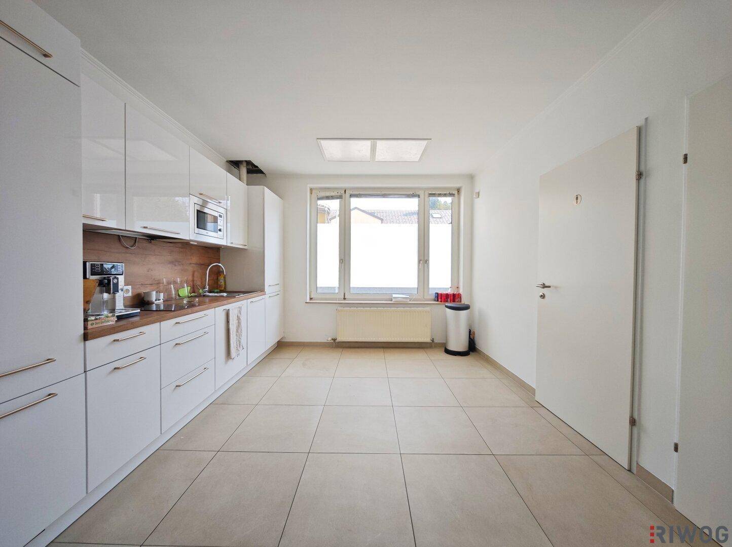 Moderne Küche mit weißen Hochglanzschränken, Holz-Arbeitsplatte und Fenster.