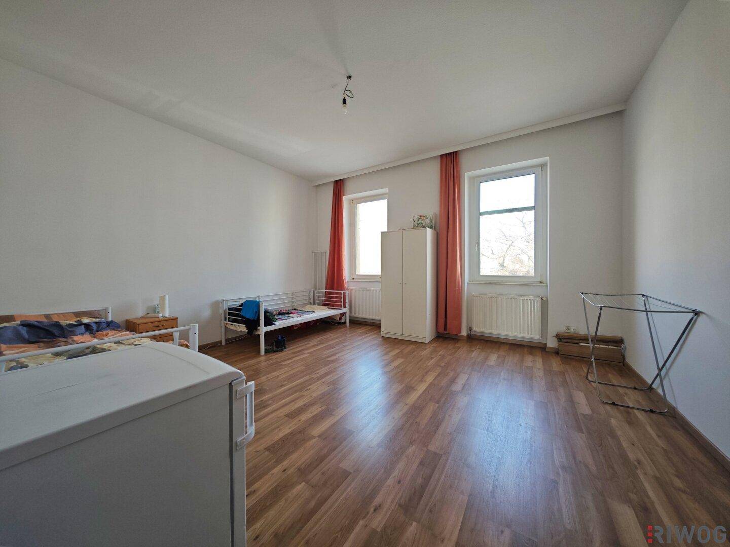 Helles Schlafzimmer mit Laminatboden, zwei Fenstern und Heizkörper.