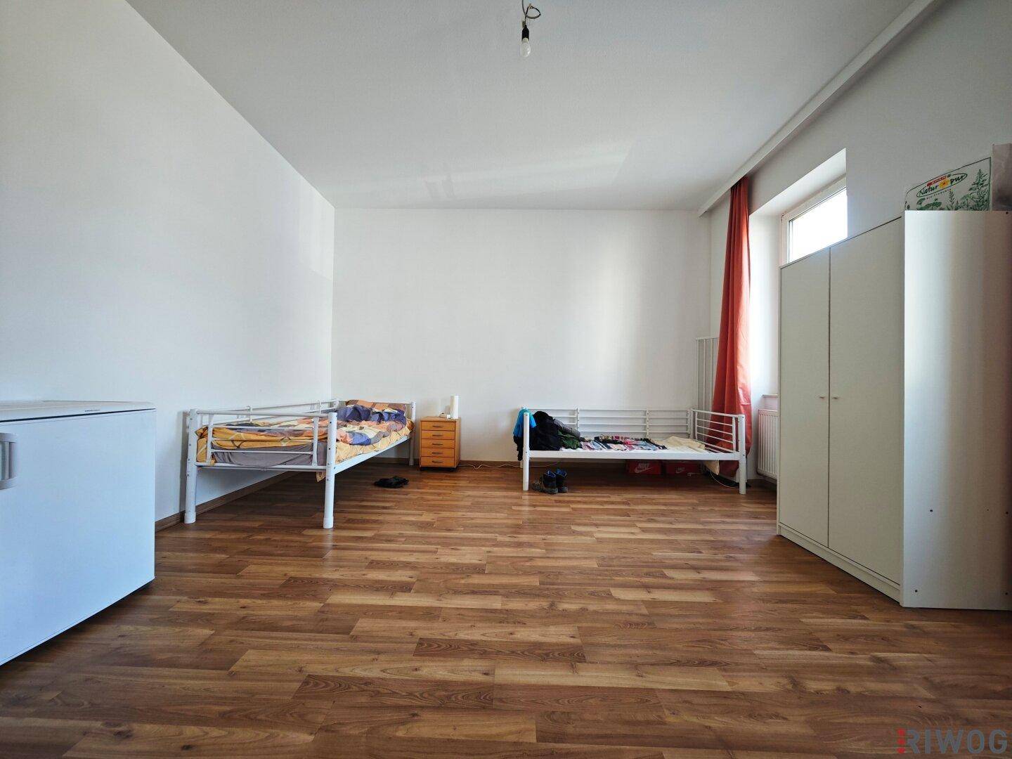 Geräumiges Schlafzimmer mit zwei Betten, Laminatboden und Fenster.