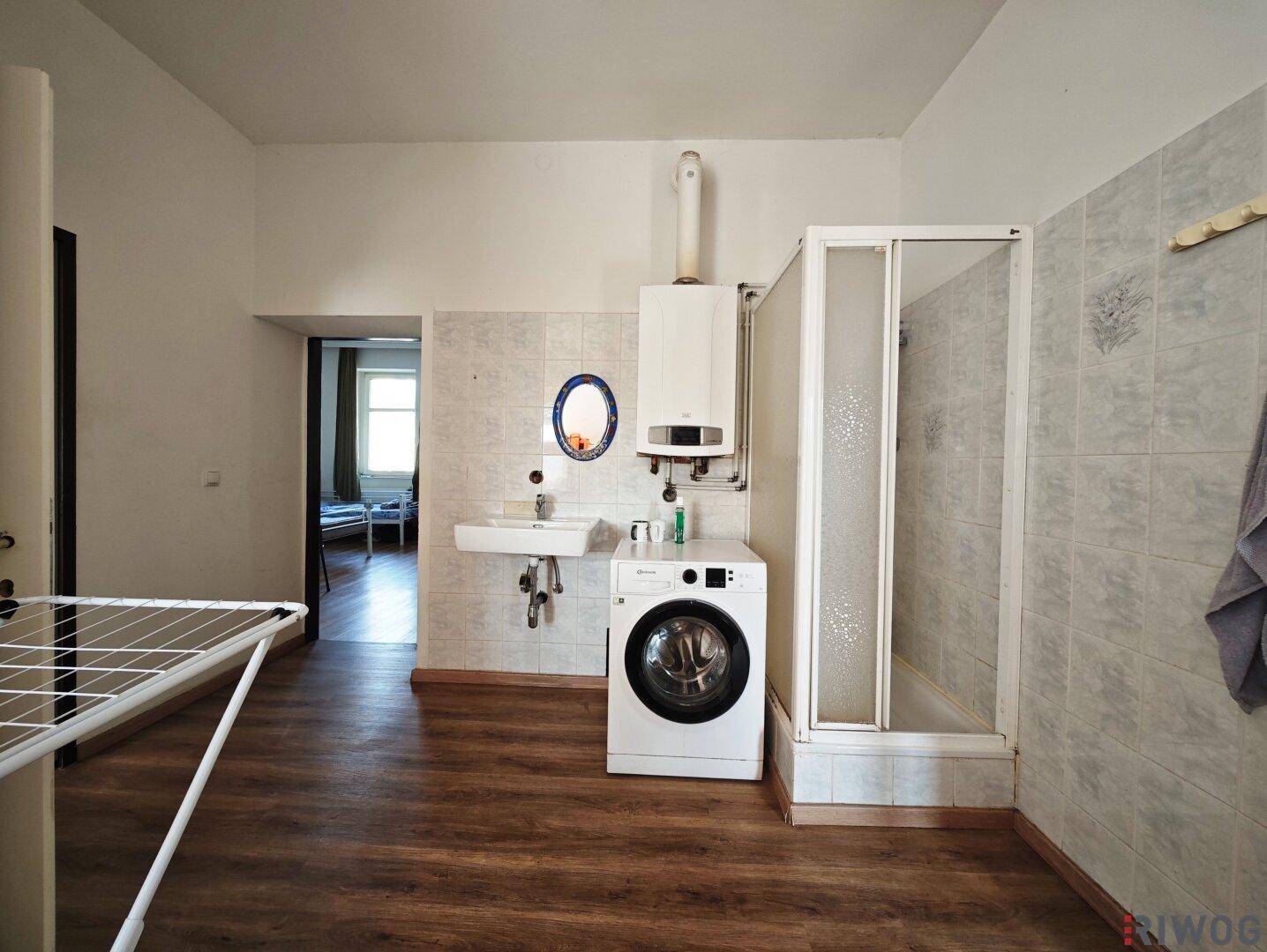 Waschraum mit Dusche, Waschbecken, Waschmaschine und Fliesenboden.