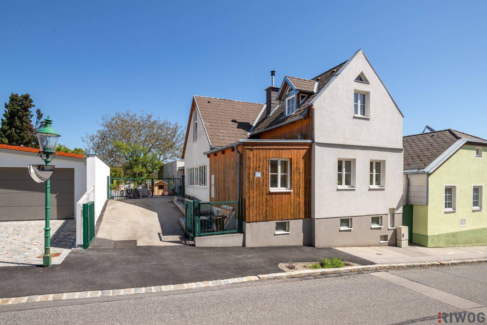 Seitenansicht des Hauses mit Holzelementen und gepflasterter Einfahrt an einem sonnigen Tag.