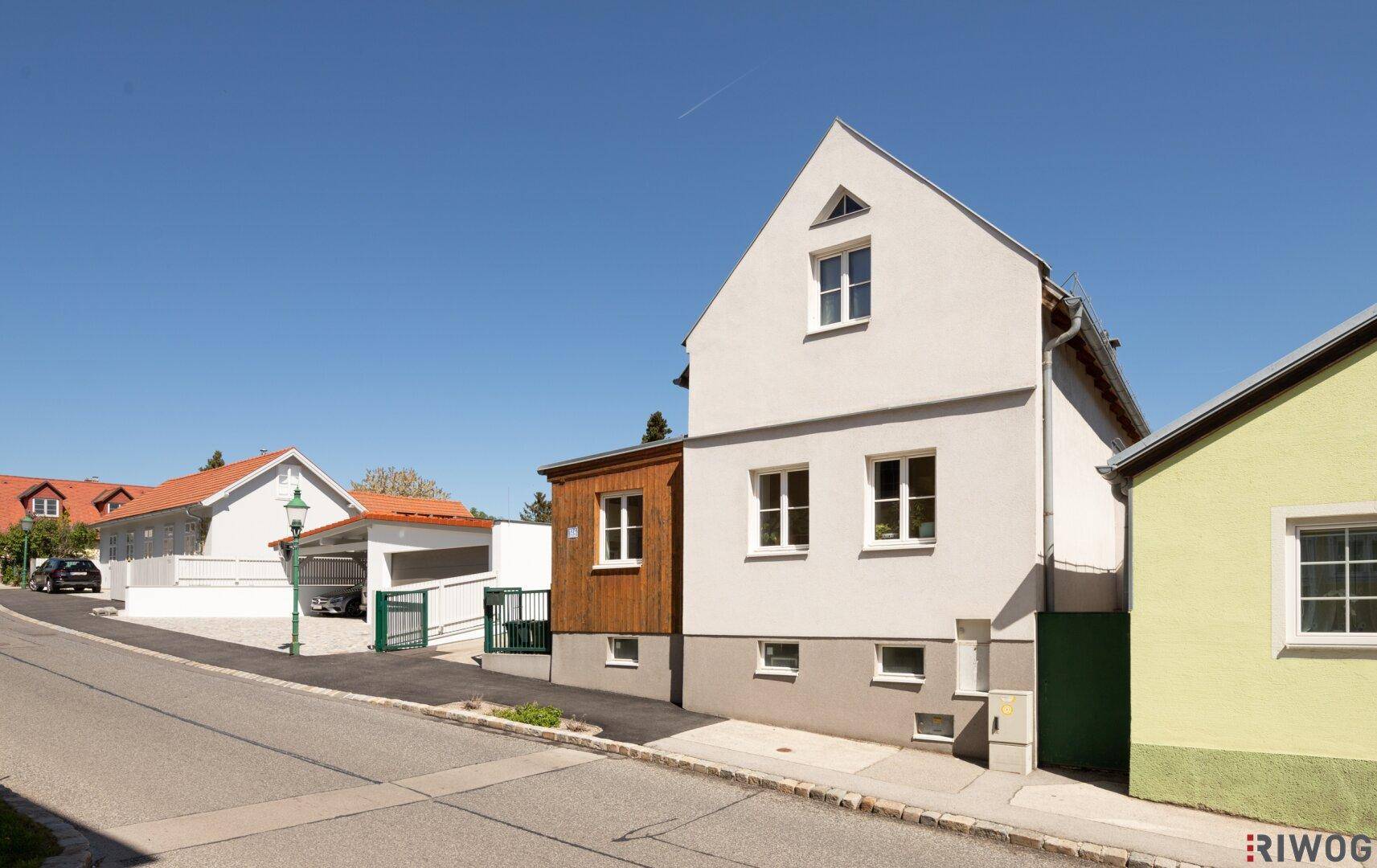Ansicht des Hauses von der Straße mit weißer Fassade und Holzakzenten unter blauem Himmel.
