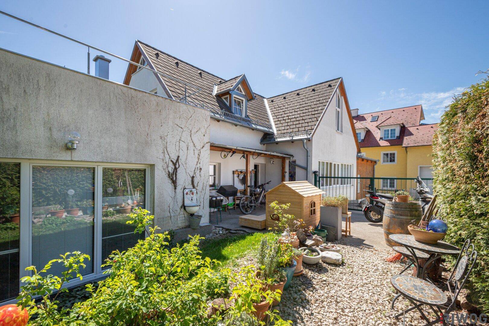 Hinterhofbereich mit Kiesfläche, Pflanzen in Töpfen und einem Grillplatz neben dem Haus.