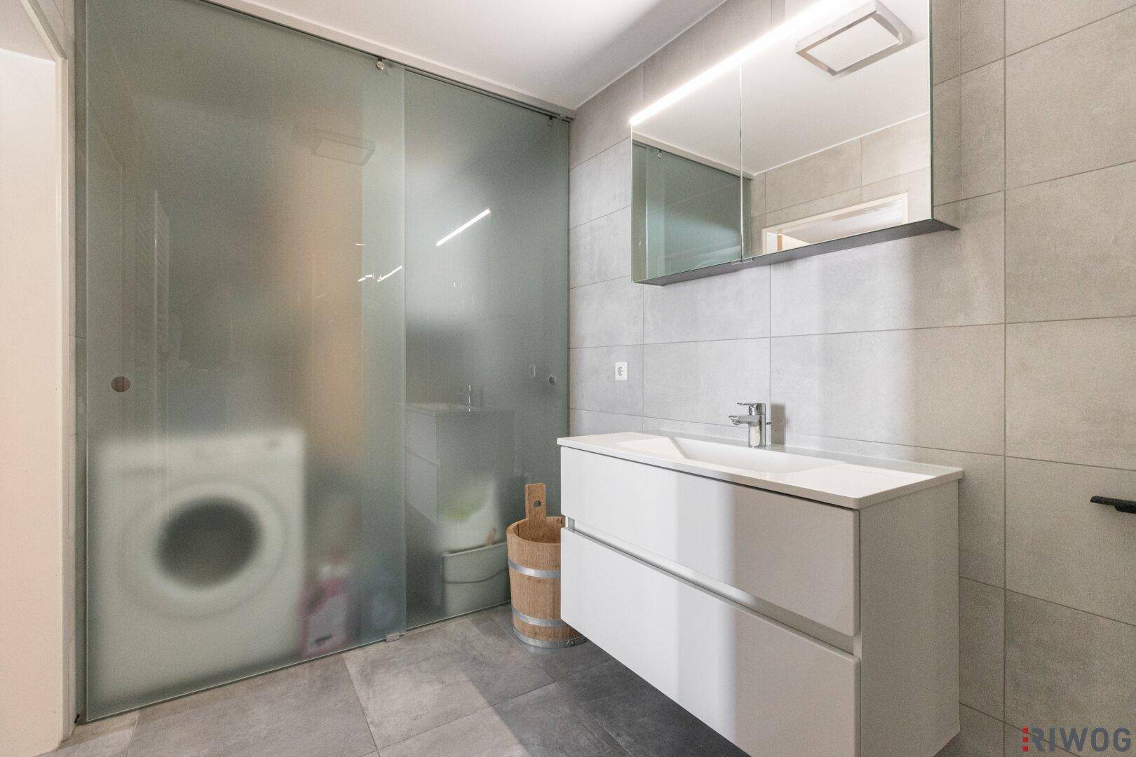 Helles Badezimmer mit Waschbecken, Spiegelschrank und abgetrenntem Bereich für die Waschmaschine.