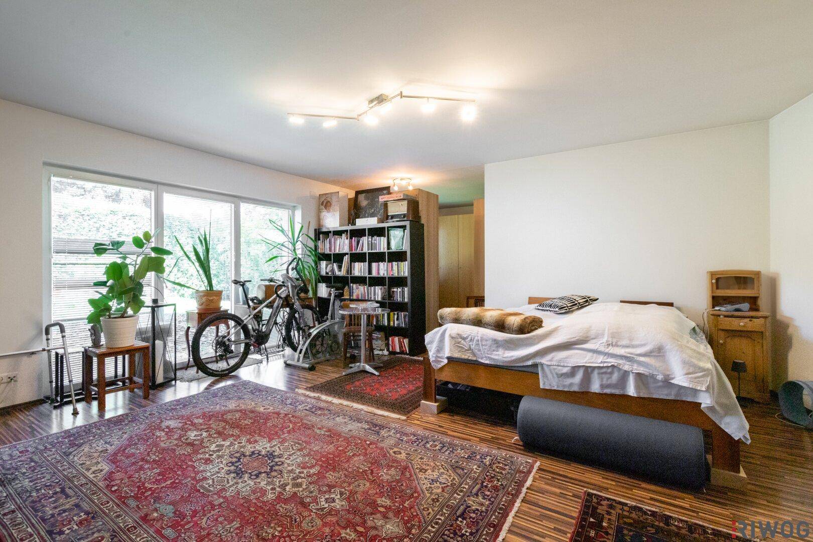 Geräumiges Schlafzimmer mit Holzboden, großen Fenstern und viel Tageslicht, eingerichtet mit Bett und Bücherregal.