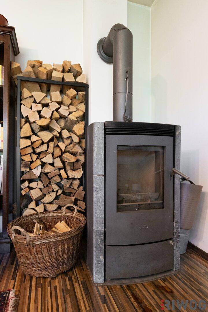 Moderner Holzofen mit gestapeltem Brennholz, der eine gemütliche Atmosphäre schafft.