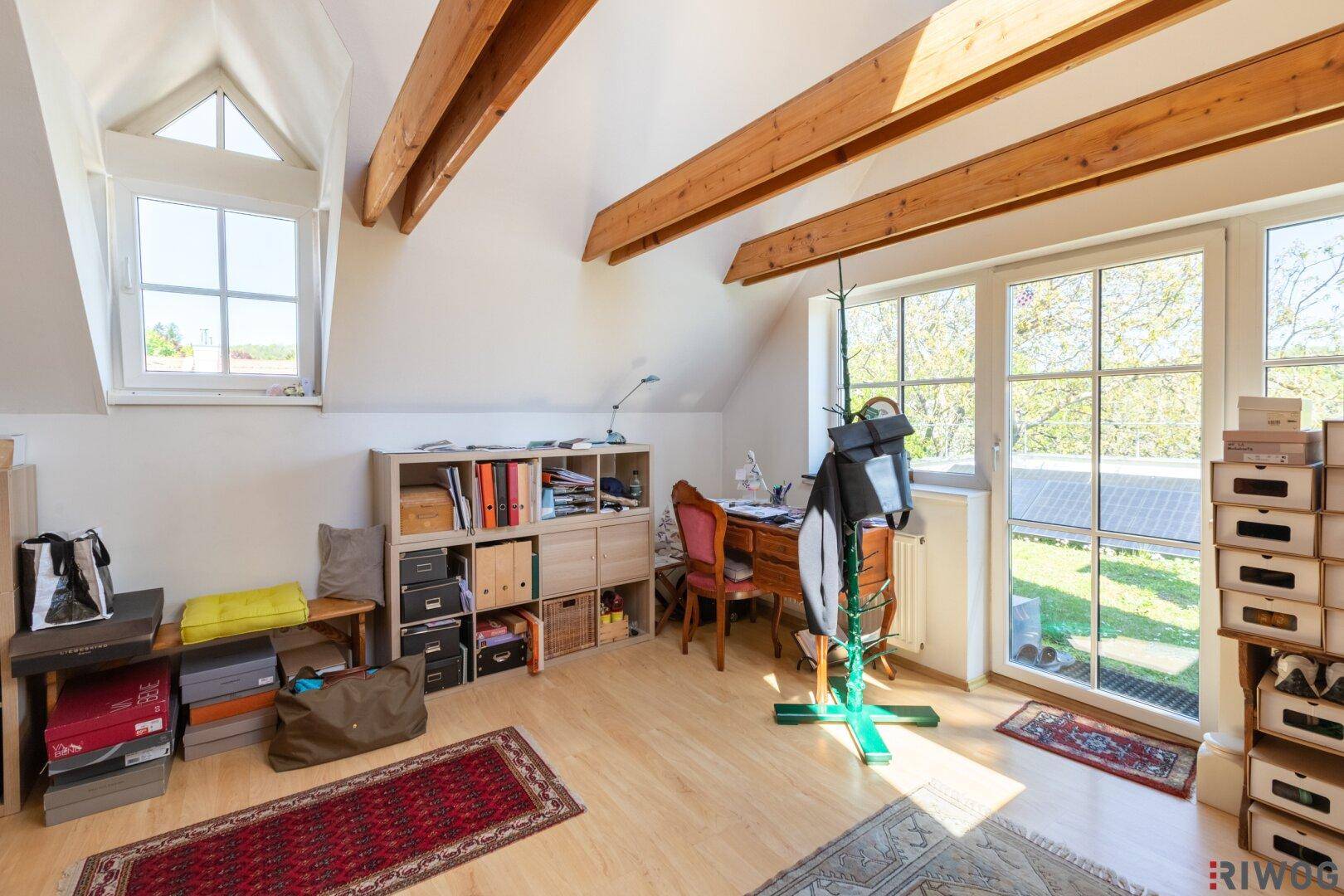 Geräumiges Arbeitszimmer mit viel Tageslicht, Holzbalken und Blick ins Grüne.