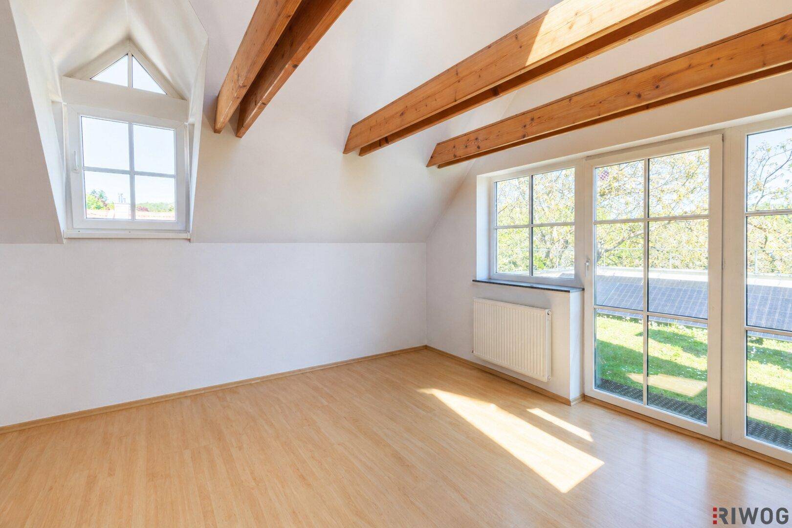Leerer Raum im Dachgeschoss mit Holzbalken, hellen Wänden und Holzboden.