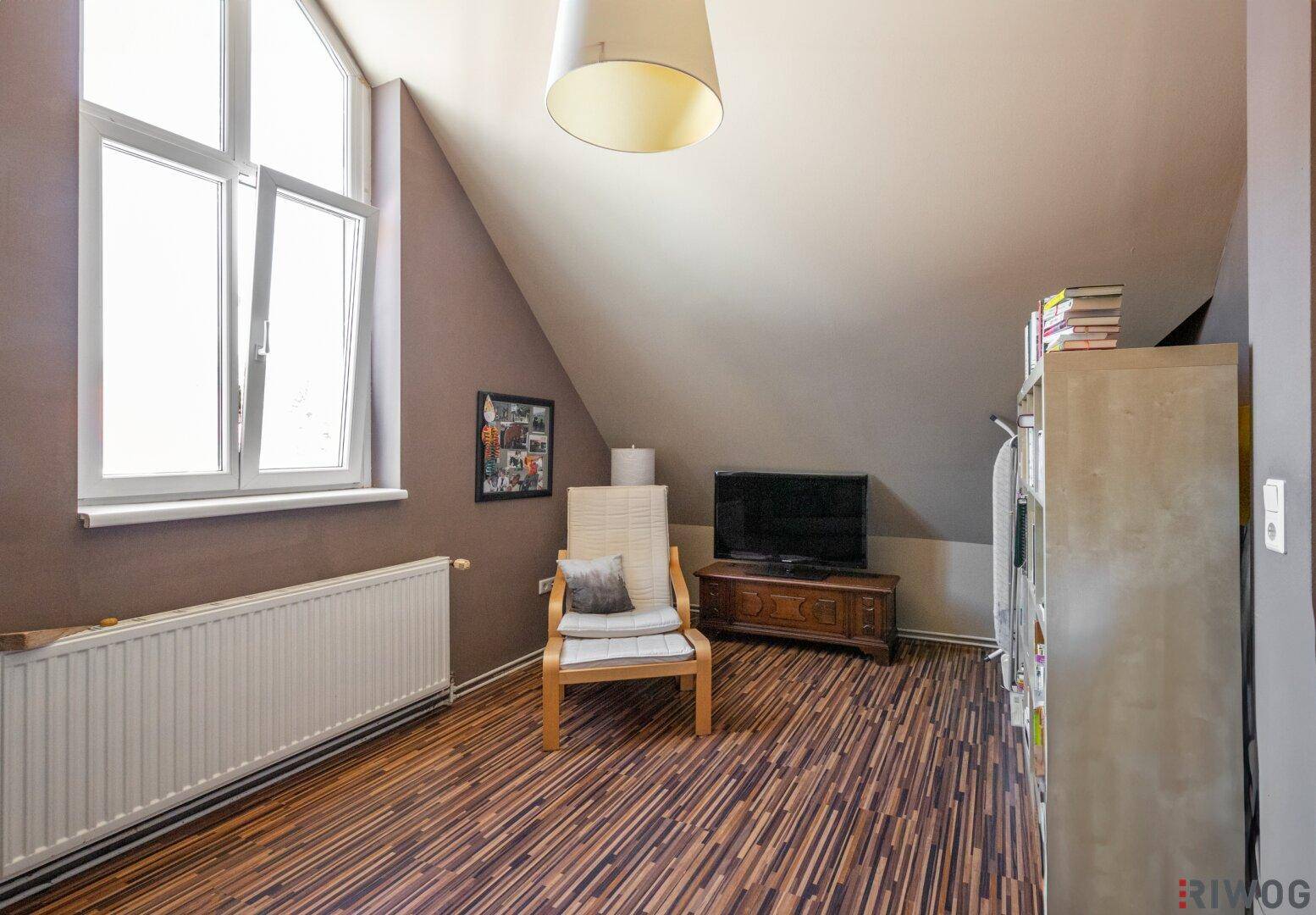 Gemütliches Zimmer im Dachgeschoss mit Schrägdach, Fernseher und Laminatboden.