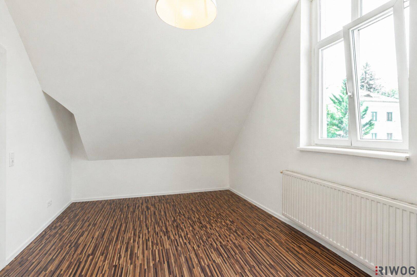 Heller Raum im Dachgeschoss mit Schrägdach, großem Fenster und Laminatboden.