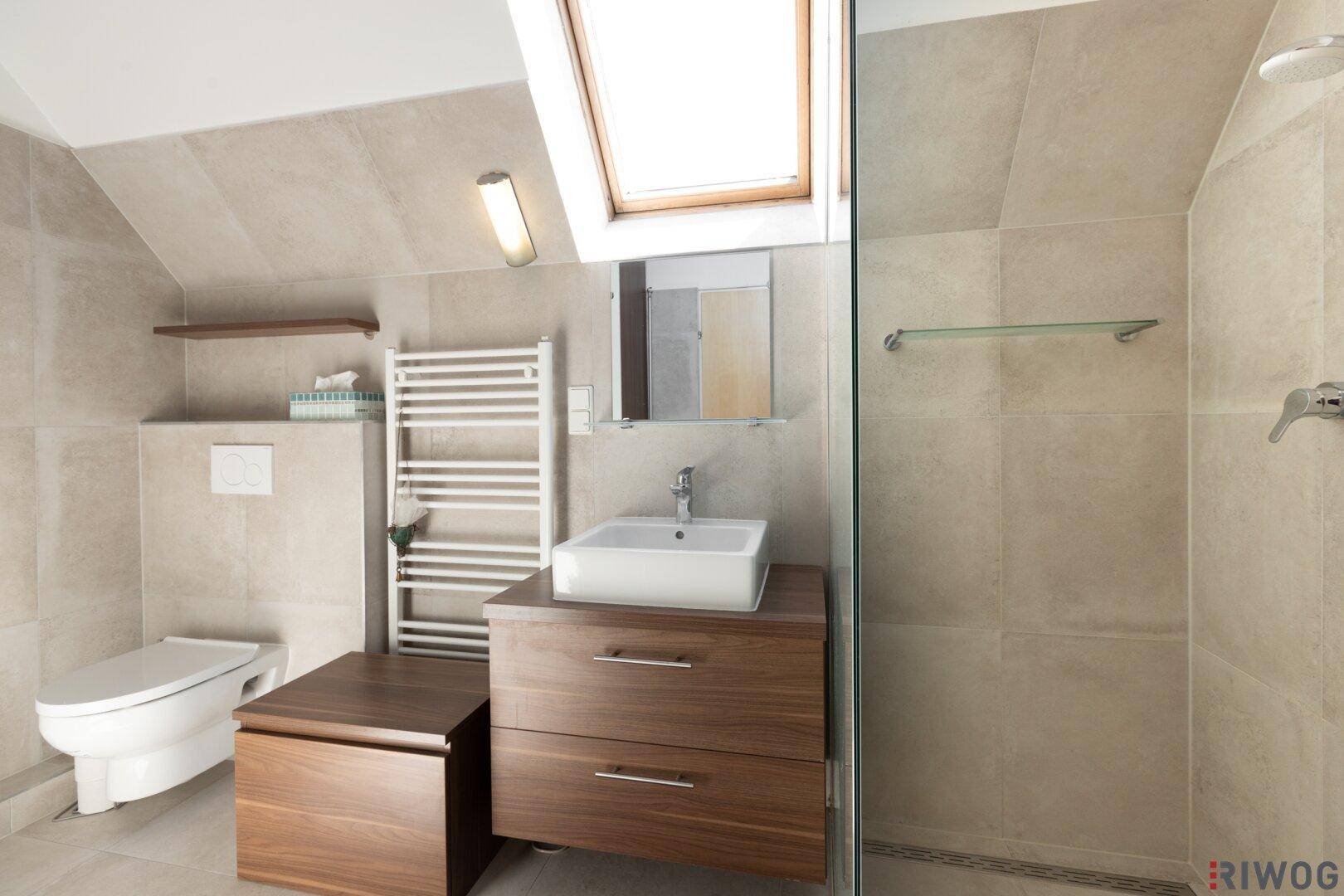 Helles Badezimmer mit Dachfenster, Dusche, WC und modernem Waschtisch.