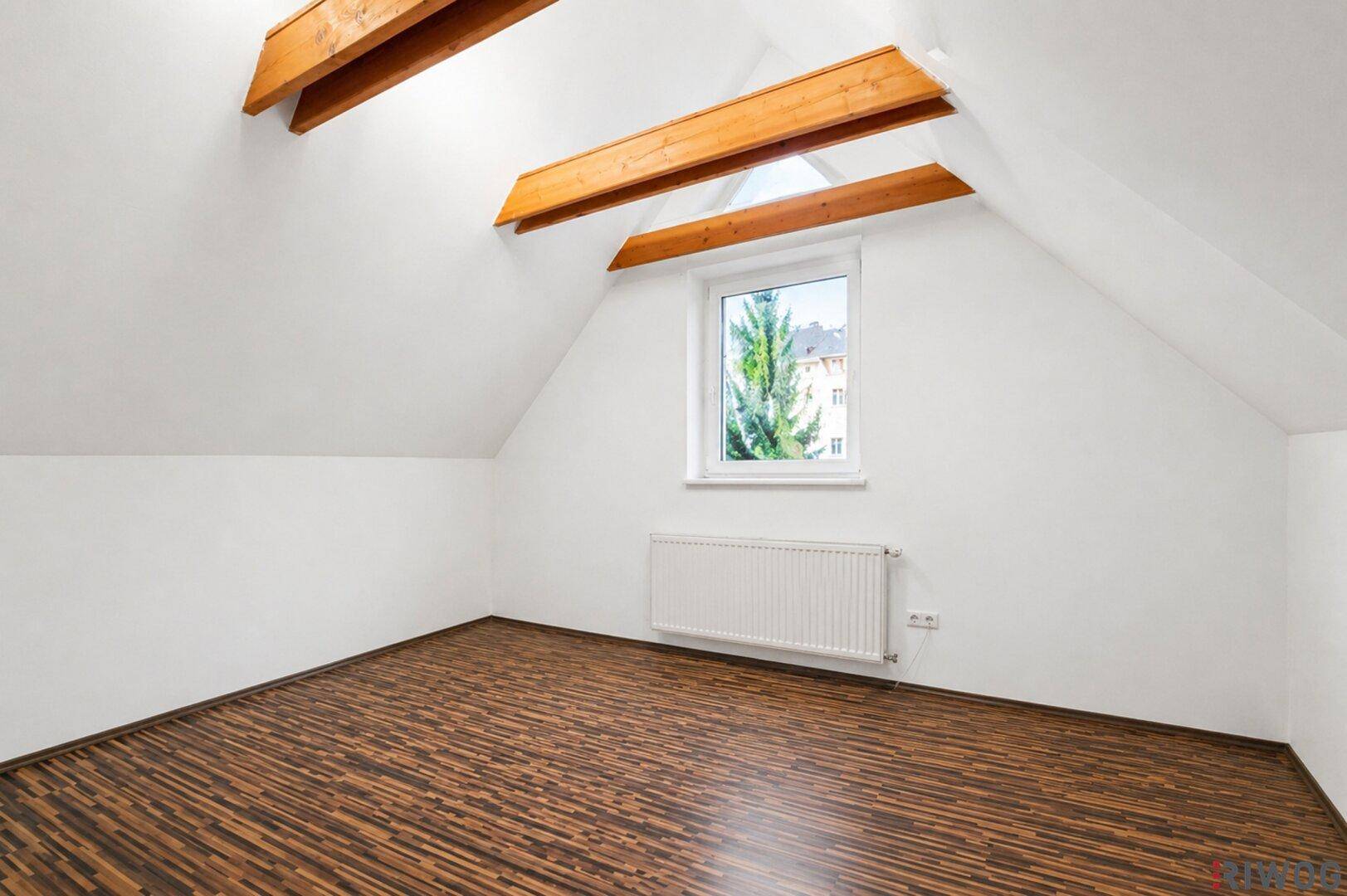 Leerer Raum im Dachgeschoss mit Holzbalken, Schrägdach und Laminatboden.