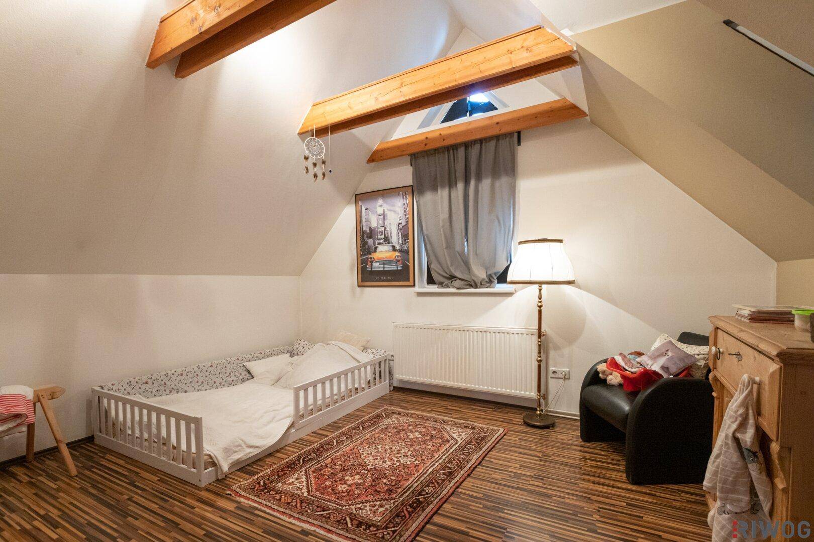 Kinderzimmer im Dachgeschoss mit Holzbalken, Schrägdach und Laminatboden.