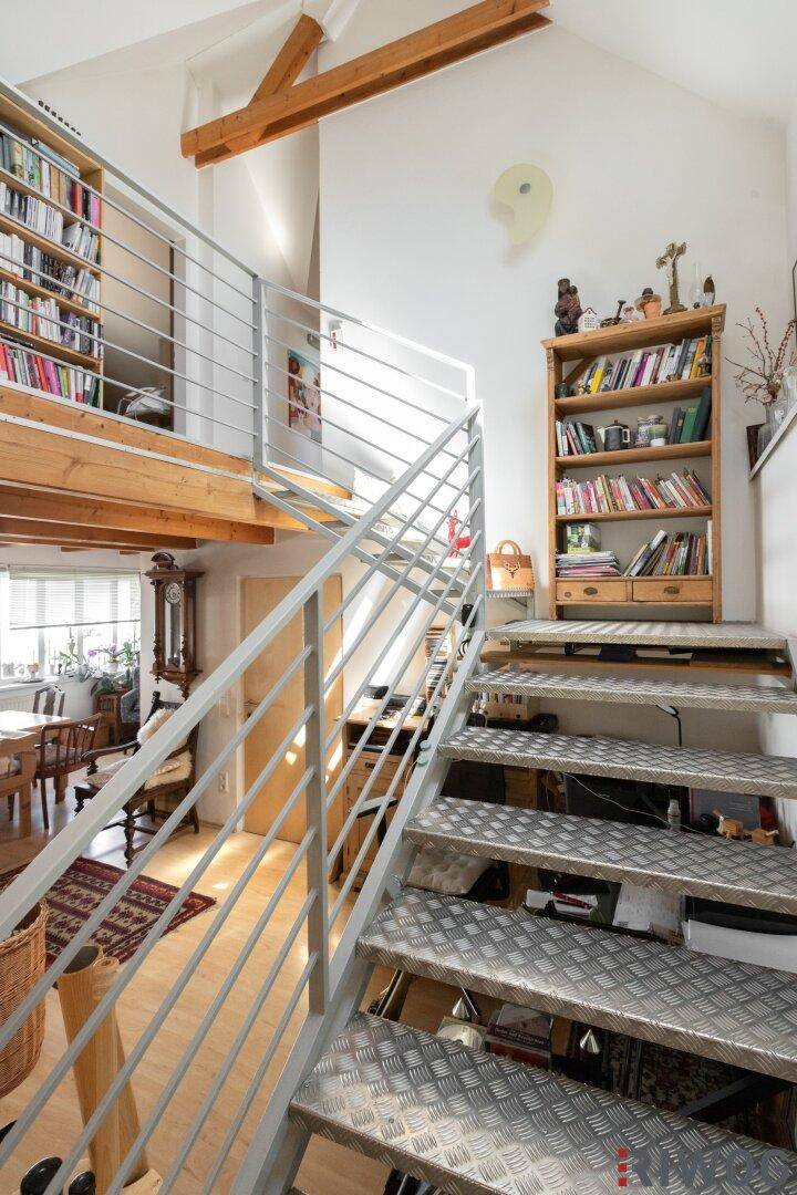 Industriell anmutende Metalltreppe führt zu einem hellen Zwischengeschoss mit Bücherregalen.
