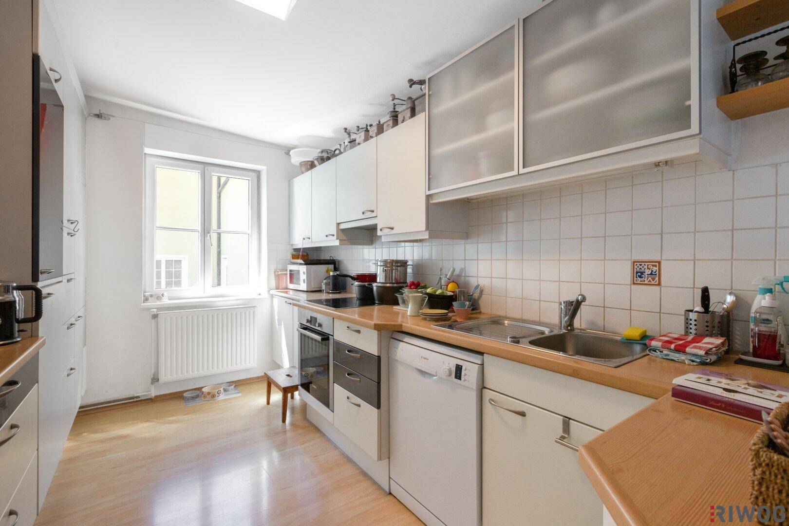 Helle Küche mit weißen Schränken, Holztheken und einem Fenster, das viel Tageslicht spendet.