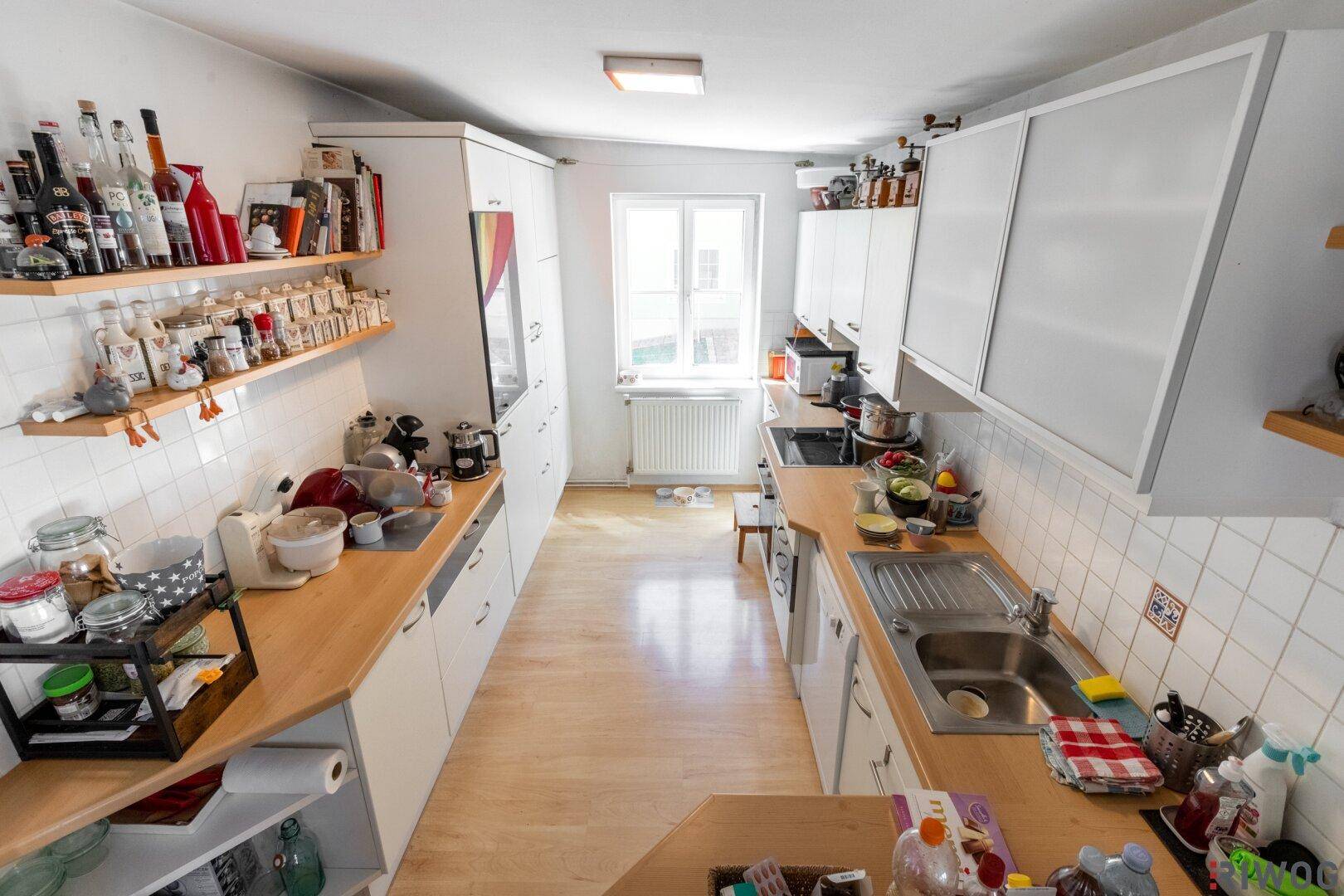 Funktionale Küche mit weißen Schränken, Holztheken und einem Fenster, gut ausgestattet für den Alltag.