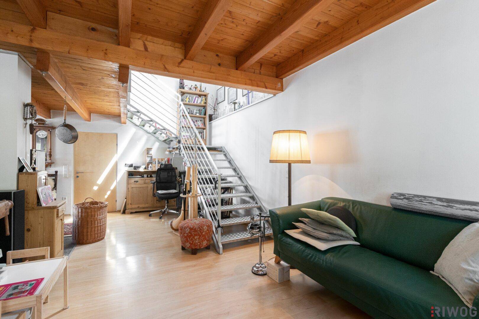 Helles Wohnzimmer mit Holzbalkendecke, Ledersofa und einer modernen Metalltreppe zum Obergeschoss.