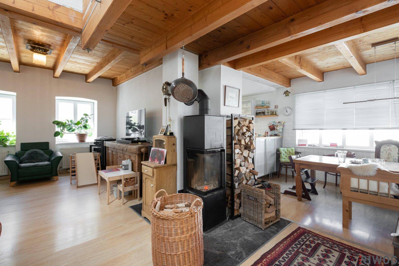 Geräumiger Wohn- und Essbereich mit Holzbalkendecke, Kaminofen und hellem Parkettboden.