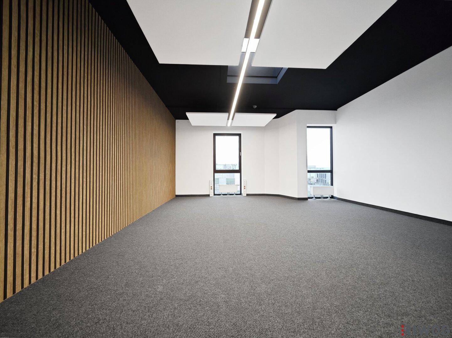 Heller Büroraum mit Teppichboden, Holzlamellenwand und großen Fenstern, ideal für moderne Arbeitsumgebungen.