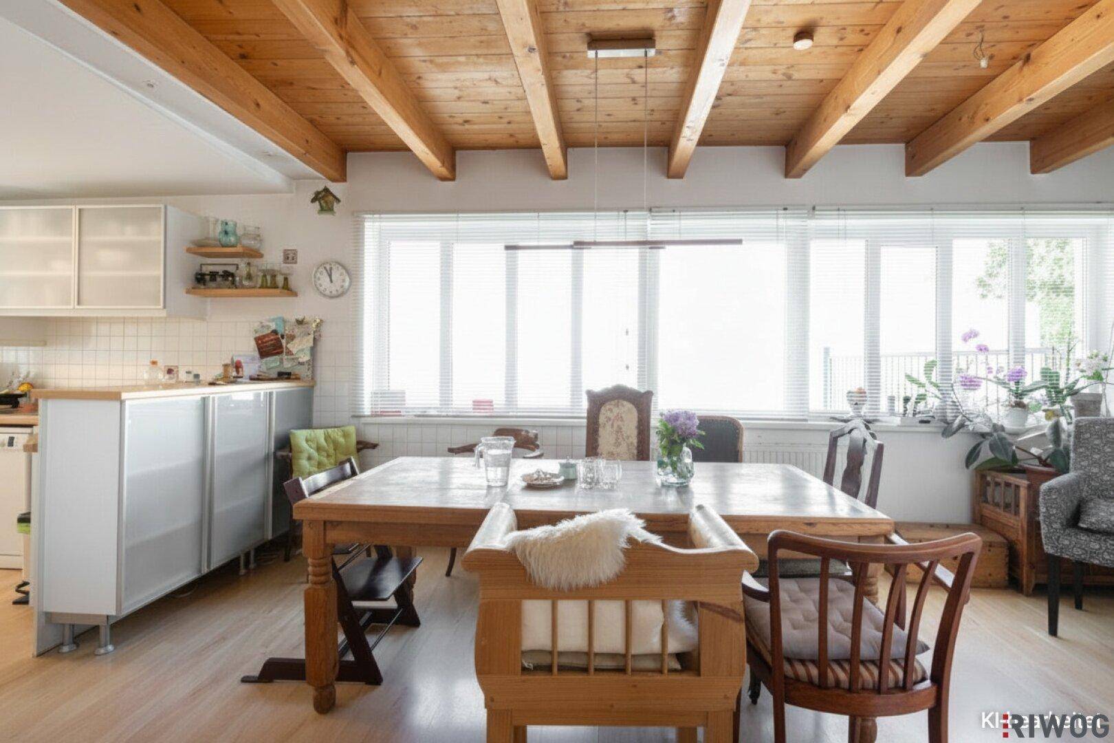 Gemütlicher Essbereich mit Holztisch, freiliegenden Deckenbalken und großen Fenstern.