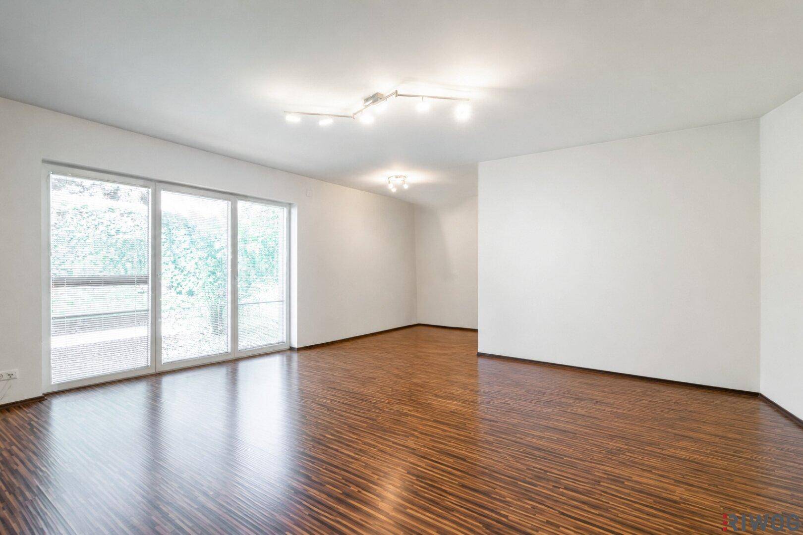 Leeres Schlafzimmer mit glänzendem Holzboden und großen Fenstern, die viel Licht hereinlassen.