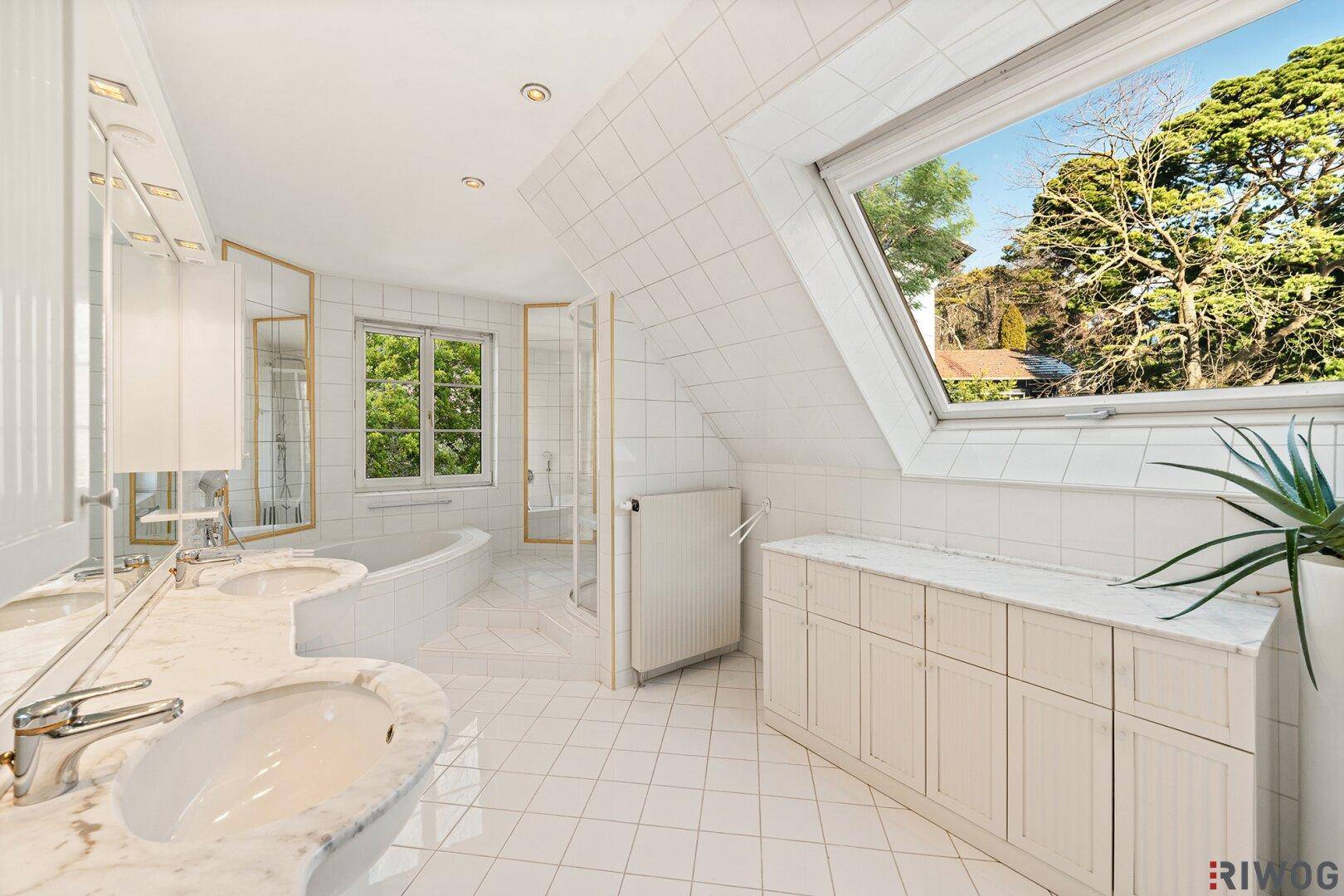 Geräumiges Badezimmer mit weißen Fliesen, Doppelwaschbecken, Badewanne und großem Dachfenster.