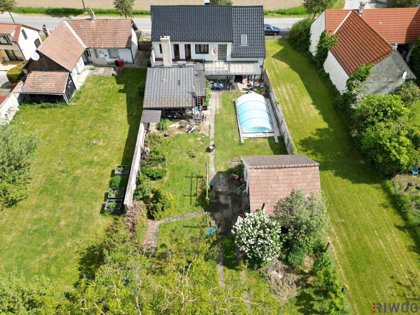 Vogelperspektive eines Hauses mit langem Garten, überdachtem Pool und Nebengebäuden.