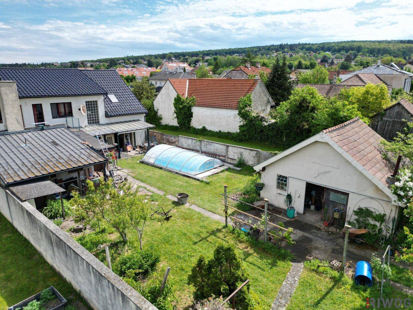 Blick auf den Gartenbereich mit Pool, Nebengebäude und dem Hauptgebäude im Hintergrund.