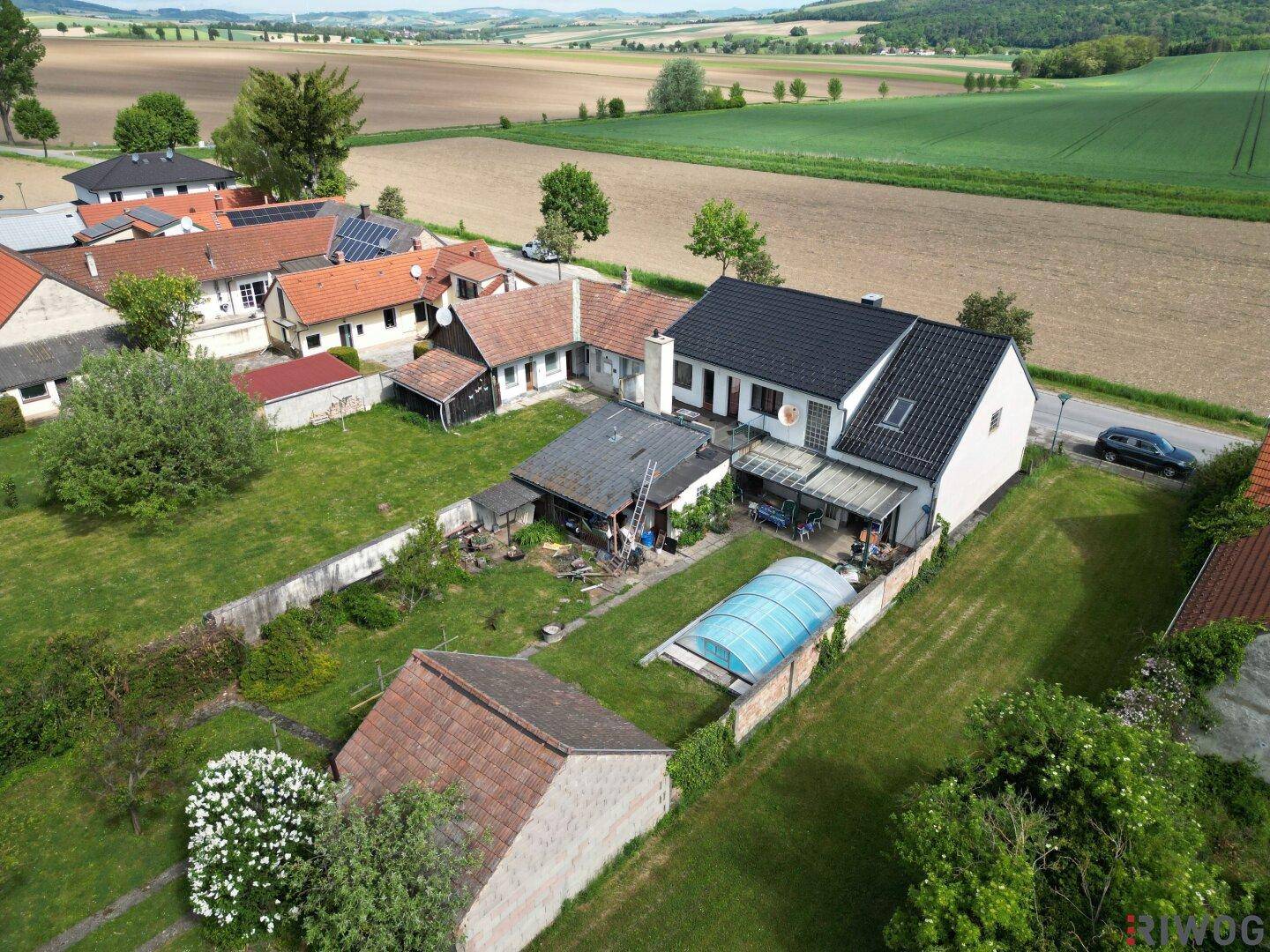 Luftaufnahme eines Wohnhauses mit Garten, Pool und angrenzenden Feldern in ländlicher Umgebung.