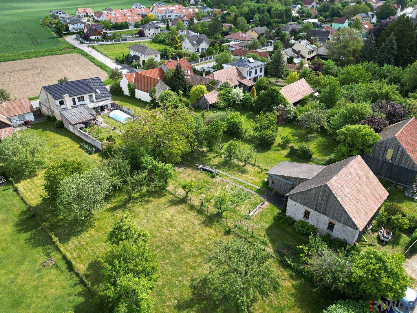 Weitläufige Ansicht eines Dorfes mit Wohnhäusern, Gärten und weiten Feldern im Hintergrund.
