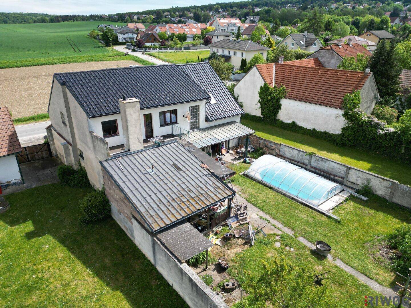 Luftaufnahme des hinteren Grundstücks mit Garten, Pool und Nebengebäuden, umgeben von einer Mauer.