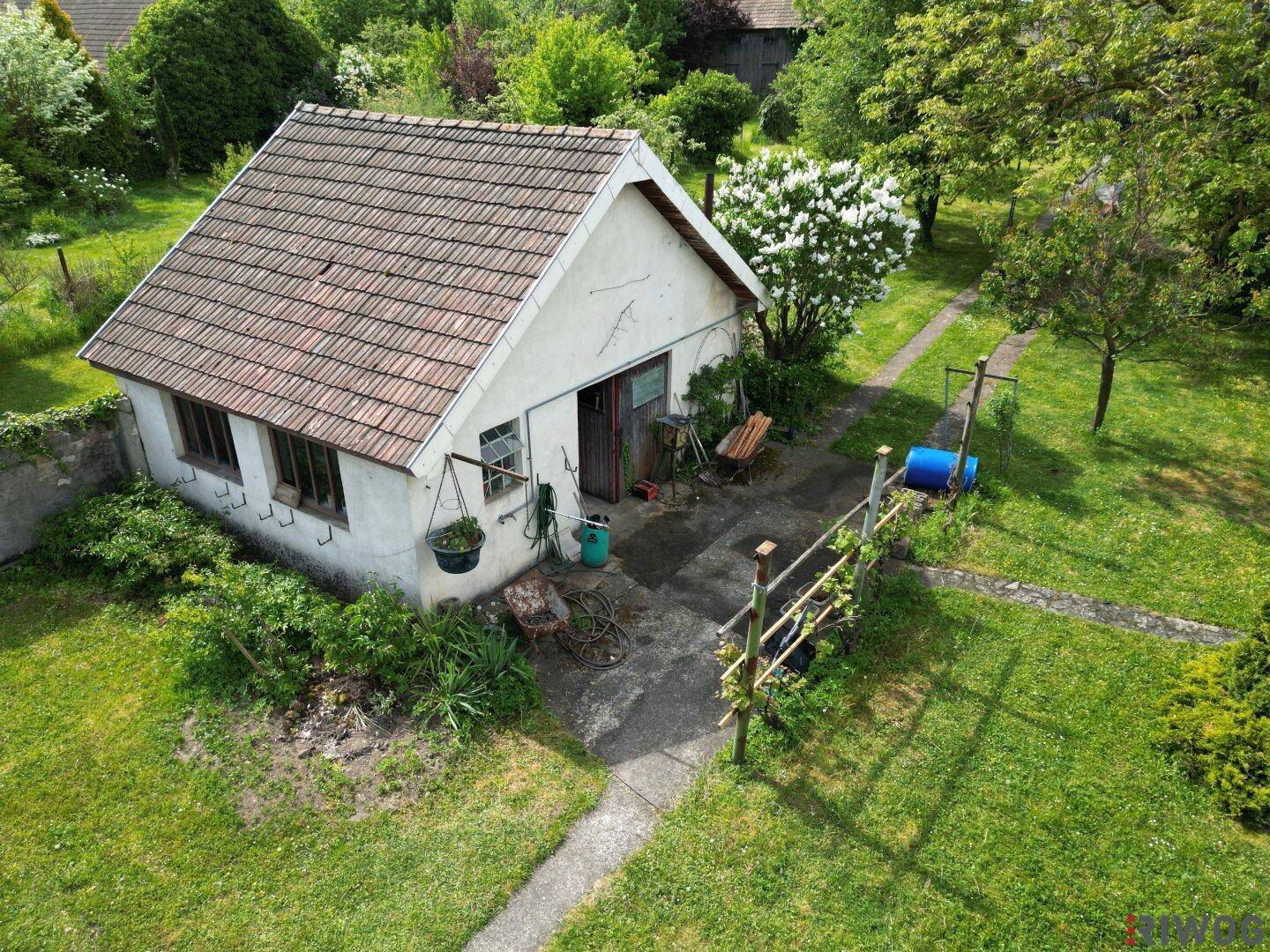 Kleines Nebengebäude im Garten mit Ziegeldach und einfacher Bauweise, umgeben von Grün.