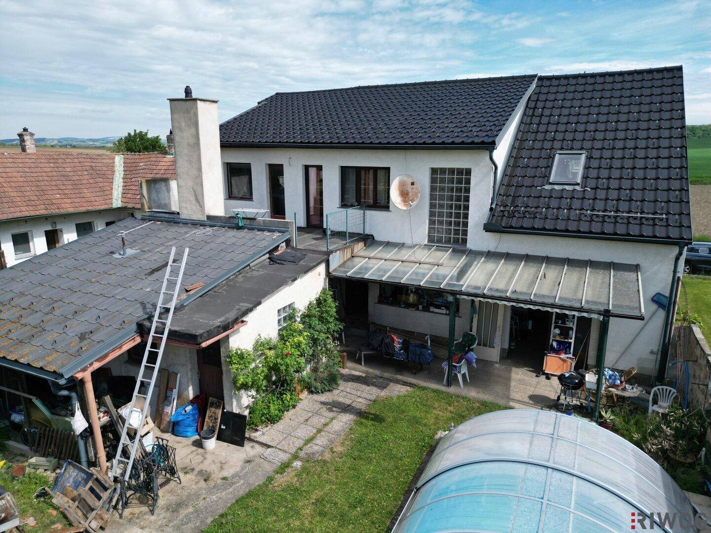 Rückseite des Hauses mit überdachter Terrasse, Pool und angrenzendem Gartenbereich.