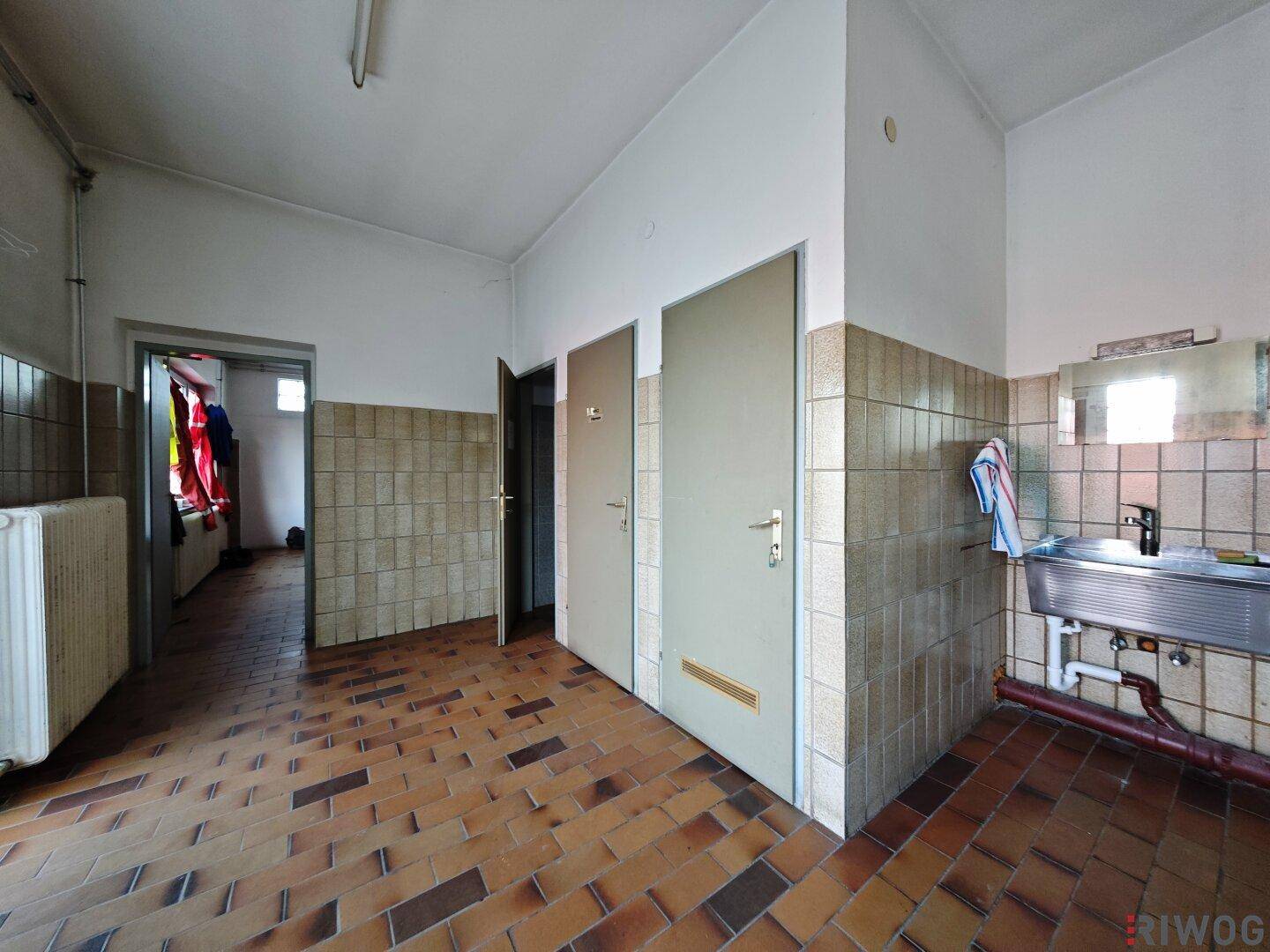 Umkleideraum oder Sanitärbereich mit gefliesten Wänden und Boden, Waschbecken und mehreren Türen.