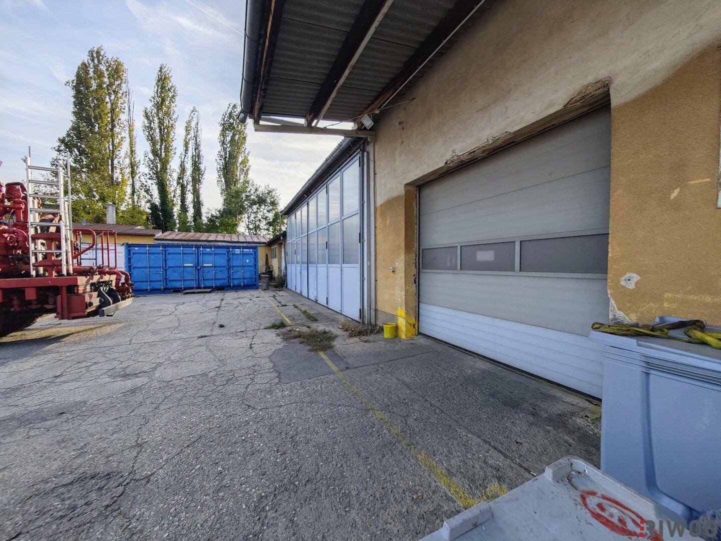 Fassade eines Industriegebäudes mit mehreren Garagentoren und Fenstern, umgeben von einer befestigten Fläche.