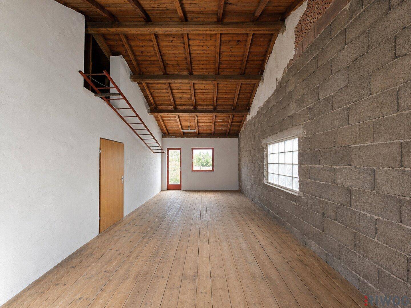 Geräumiger, leerer Raum mit Holzbalkendecke und unverputzter Ziegelwand, ideal für Ausbauprojekte.