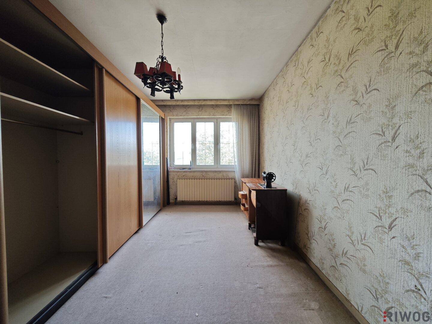Schlafzimmer mit Teppichboden, Einbauschrank und Fenster, das viel Tageslicht hereinlässt.