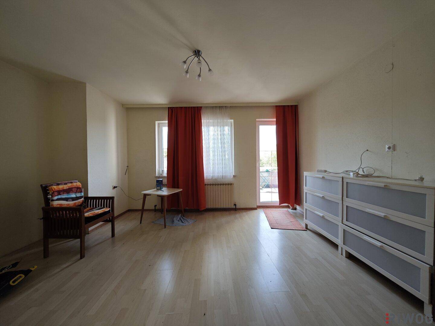 Helles Wohnzimmer mit Laminatboden und Zugang zu einem Balkon oder einer Terrasse, ideal für Entspannung.