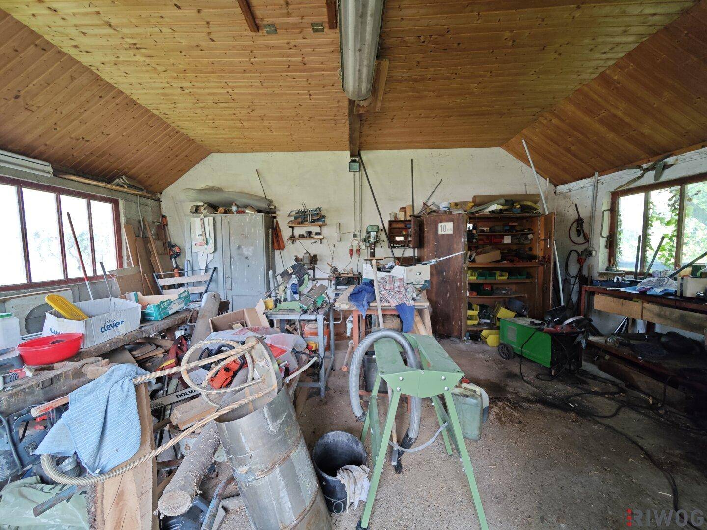 Geräumige Werkstatt mit Holzdecke und Betonboden, ausgestattet mit Werkbänken und verschiedenen Geräten.
