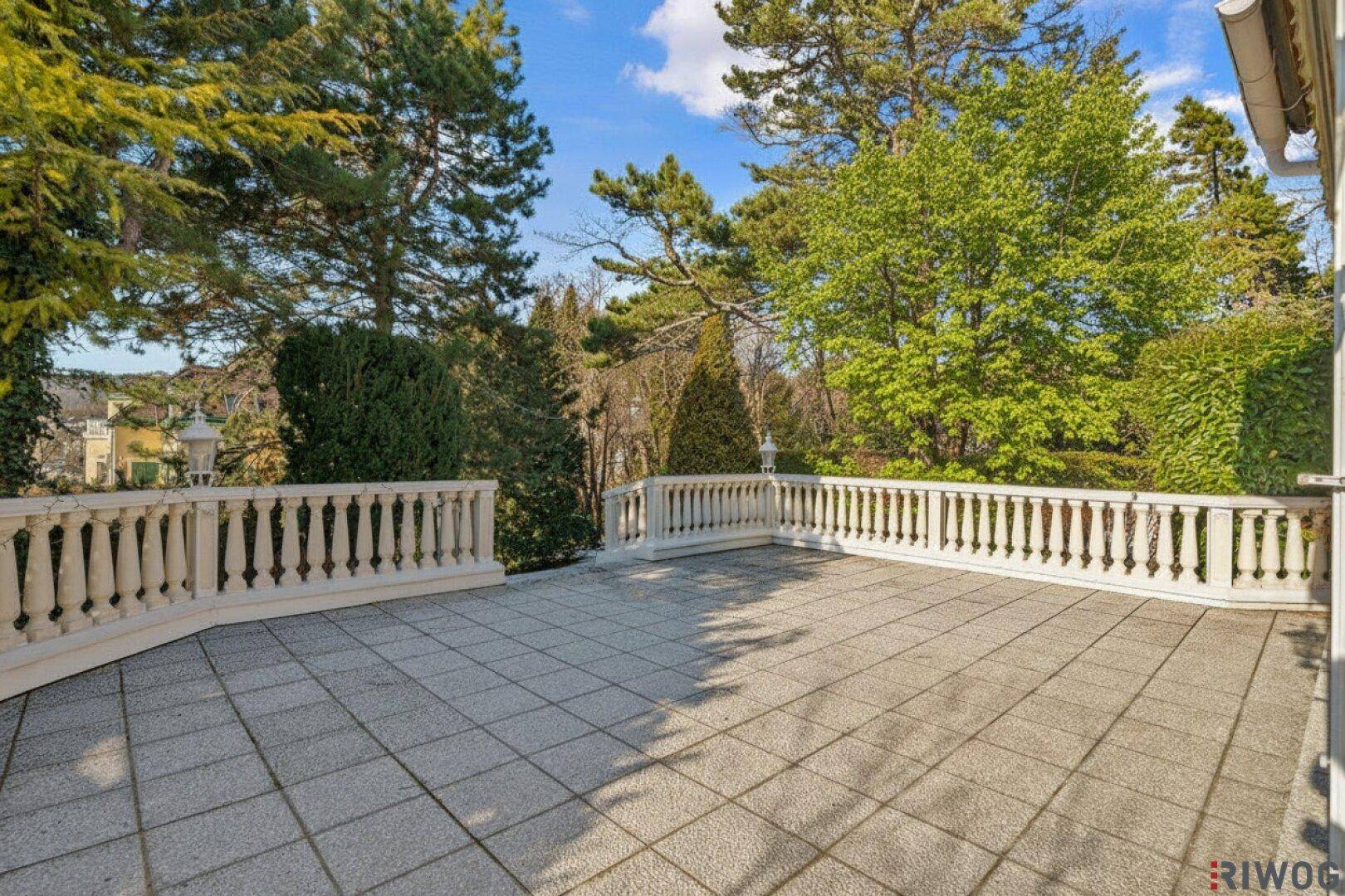 Weitläufige gepflasterte Terrasse mit klassischer Balustrade und Blick ins Grüne.