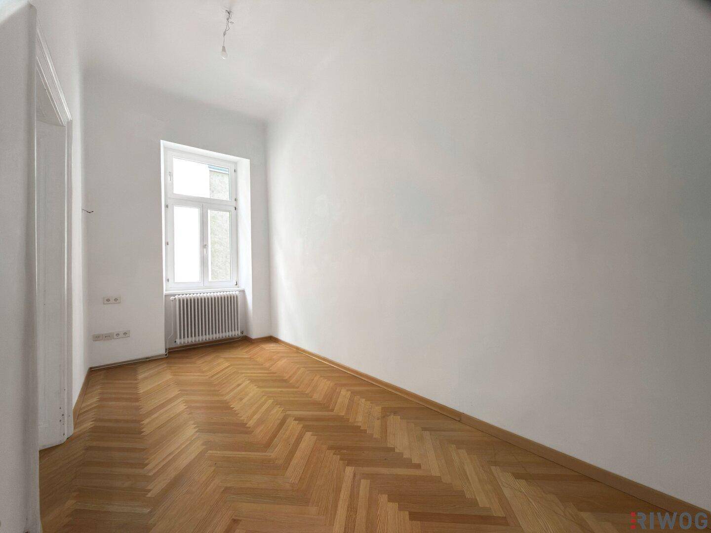 Ruhiges Schlafzimmer mit Fischgrätparkett und einem Fenster, das viel Tageslicht hereinlässt.
